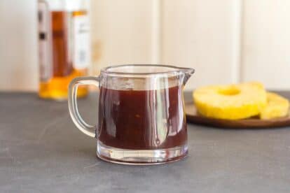 Low FODMAP Pineapply Whiskey BBQ Sauce in small glass pitcher; pineapple slices in background