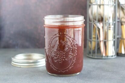 Low FODMAP sweet and sticky BBQ sauce in open mason jar, lid on the side; dark counter