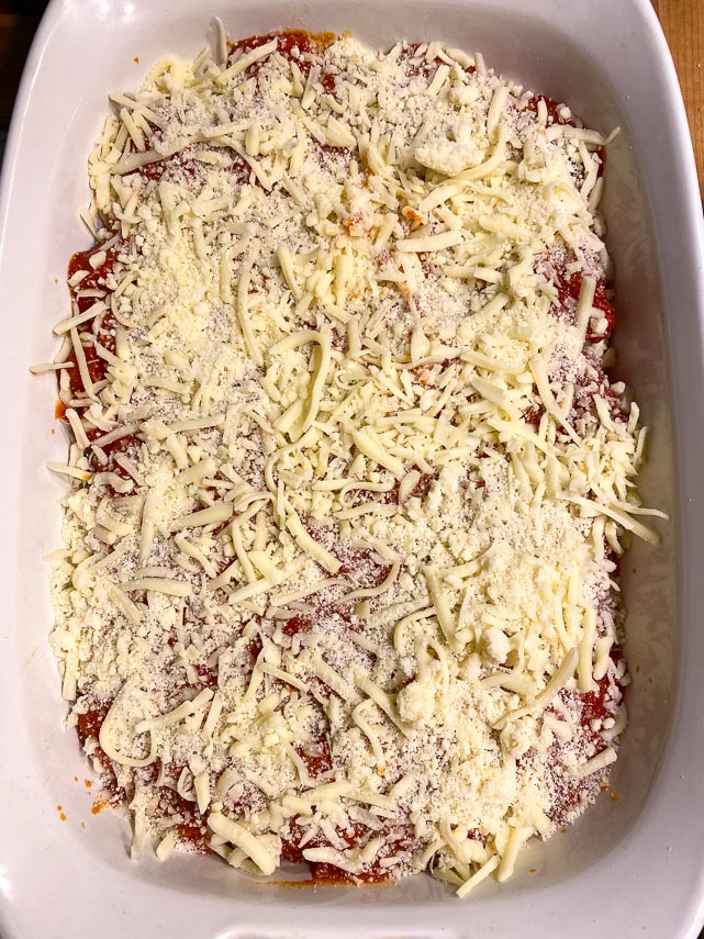 Manicotti covered with sauce and cheese, ready to go in oven
