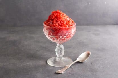 Strawberry Granita in a clear glass footed dish with a silver spoon on a dark gray background