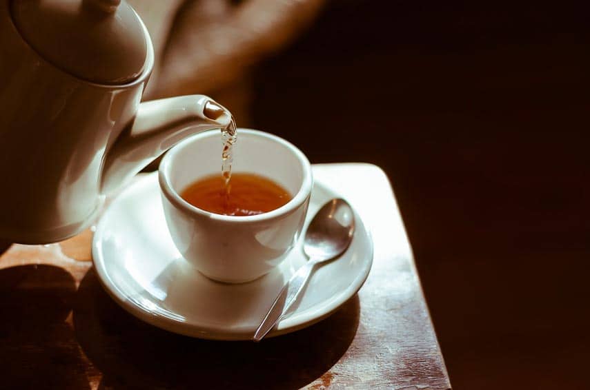 Tea being poured out of white teapot into white teacup