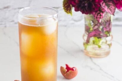 vertical image of Low FODMAP Iced Black tea with Lychees in tall clear glass; white background and magenta flowers in a small vase