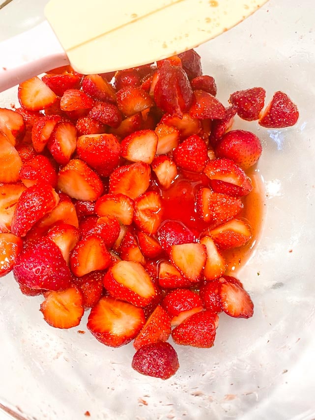 cut strawberries combined with sugar in glass bowl