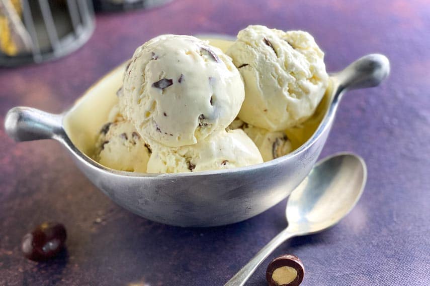 horizontal image of silver dish of low FODMAP No Churn Vanilla Ice Cream with Chocolate Covered Almonds on purple backdrop