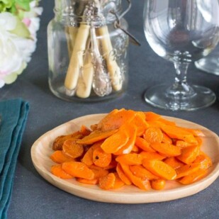 low FODMAP sauteed carrots on wooden plate; wine glass in background