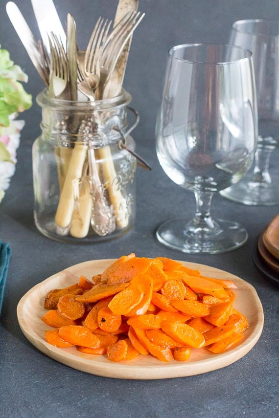 low FODMAP sauteed carrots on wooden plate; wine glass in background; vertical image