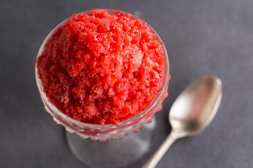 overhead closeup shot of strawberry granita in a glass dish with silver spoon