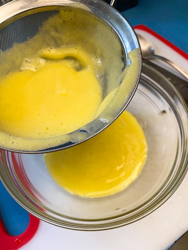 pouring liquified pineapple through a strainer; seeing juice below in bowl