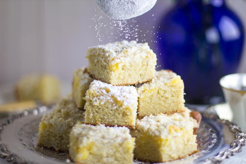 sprinkling powdered sugar on top of Low FODMAP Lemon Crumb Cake on a silver platter