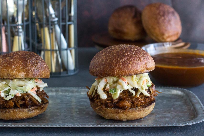 two low FODMAP BBQ Pork Sliders on a metal tray; sauce in background in glass dish