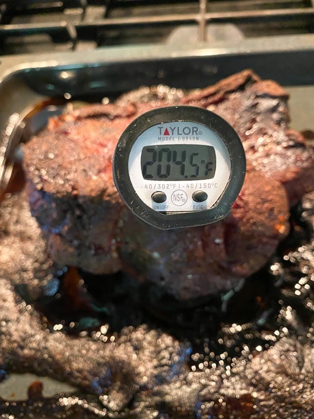 using an instant read thermometer in pork shoulder, showing 204°F