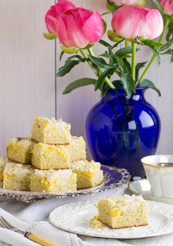 vertical image of Low FODMAP Lemon Crumb Cake on a silver platter and on white plate; coffee cup in background