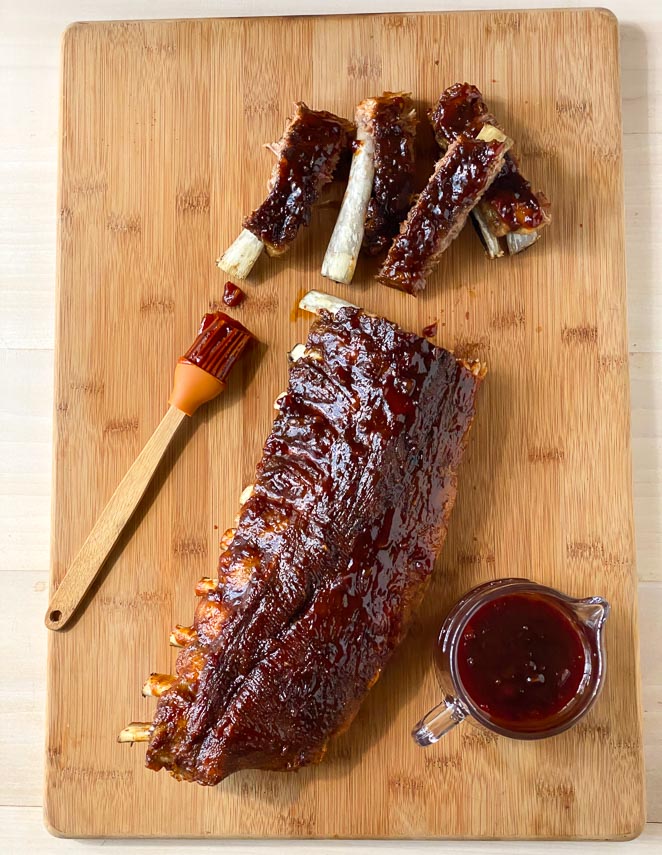 vertical image of Low FODMAP Pineapple Whiskey BBQ ribs on board with extra sauce in pitcher