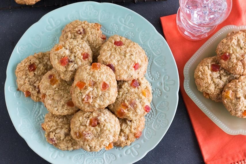 Aqua plate holding a pile of oatmeal cookies dotted with dried papaya; dark surface, glass of water on the side