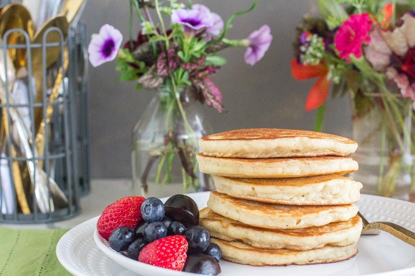 Fluffy pancakes, waiting for syrup, on a white plate with fruit on the side