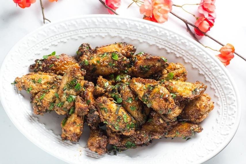 Low FODMAP Pok Pok Chicken Wings on oval white plate with coral colored flowers in background