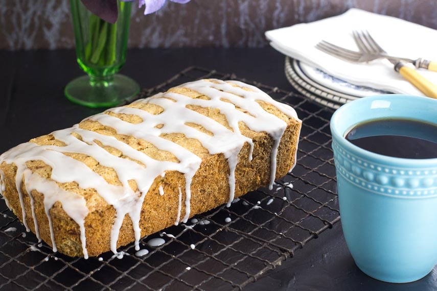Low FODMAP lemon Zucchini loaf with drizzled glaze on top on a cooling rack; dark surface and an aqua coffee mug