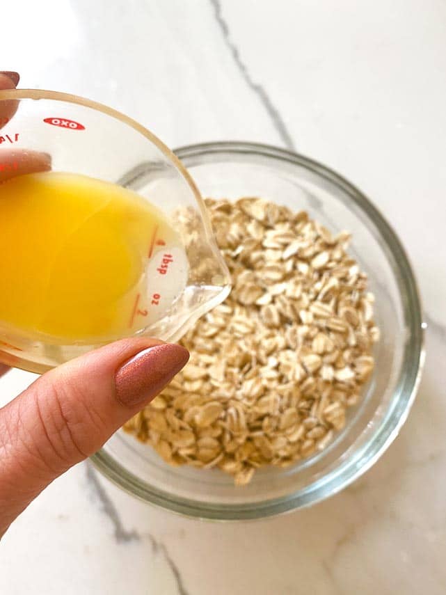 adding orange juice to oats in a clear bowl