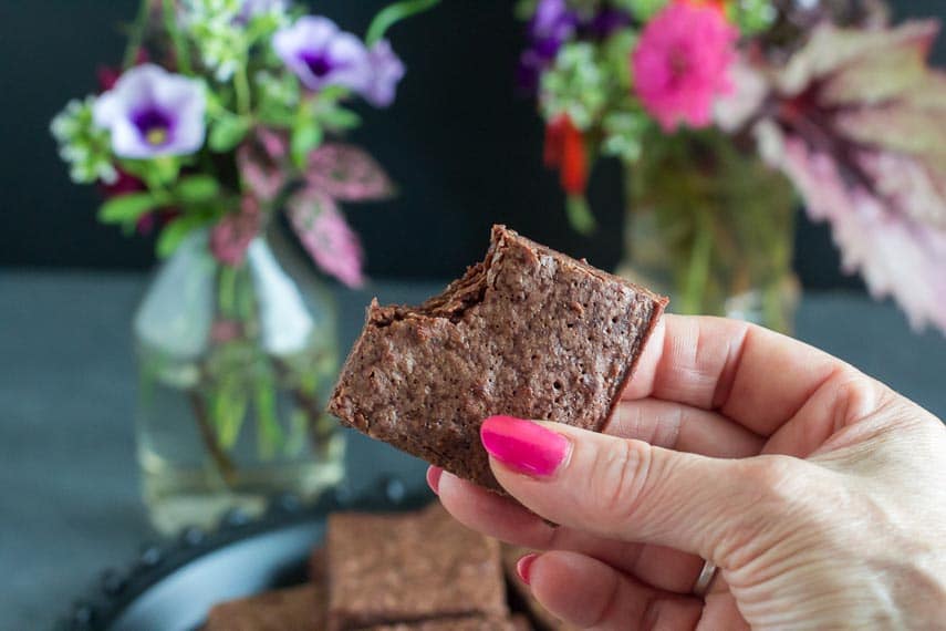 closeup image of one bowl brownie held in hand, bite taken out; flowers in background