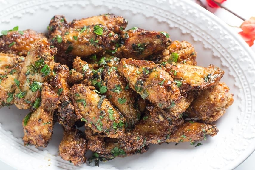 closeup of Low FODMAP Pok Pok Chicken Wings on oval white plate with coral colored flowers in background