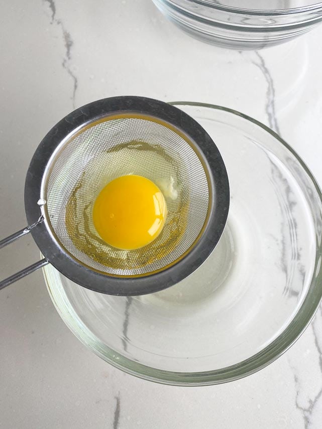 egg in fine meshed strainer over bowl, draining watery egg white, readying egg for poaching