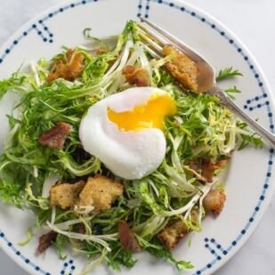 frisée salad with poached egg (broken open) on white plate with blue border