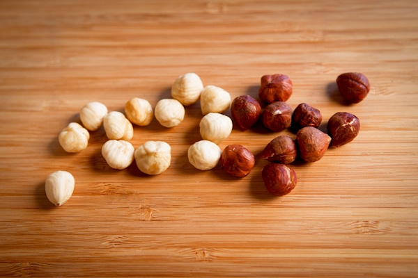 hazelnuts on a wooden board; skinned on the left; skin intact on the right
