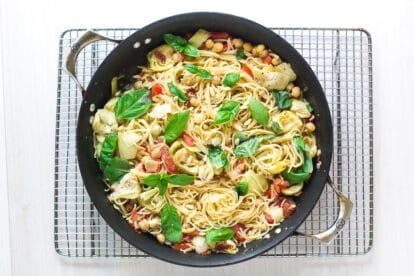 overhead image of pasta dish with chickpeas, tomatoes and artichokes in a pan on a cooling rack
