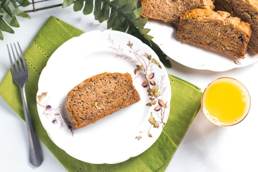 overhead of slice of zucchini banana bread on white bread; glass of orange juice alongside