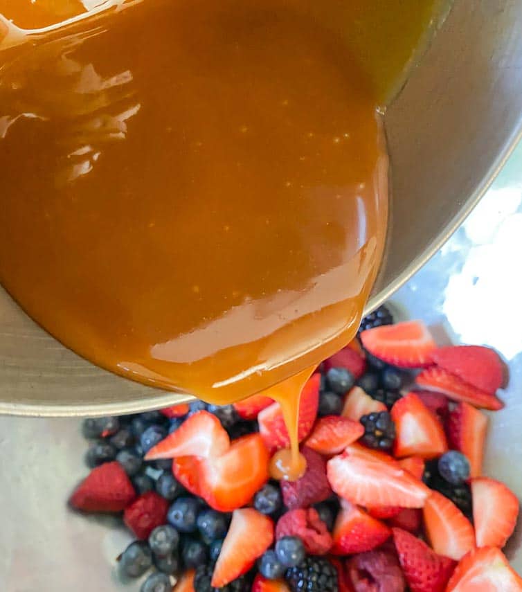 pouring caramel over berries in bowl