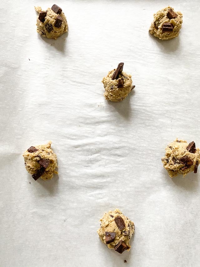 spacing chocolate chunk cookie dough out on parchment lined baking sheet pan