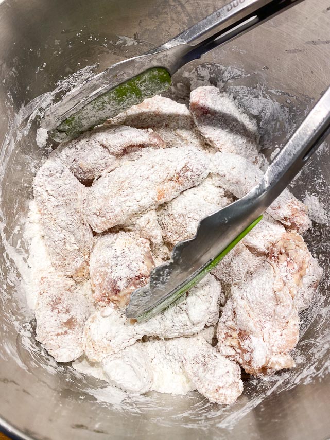 tossing chicken wings in cornstarch with tongs