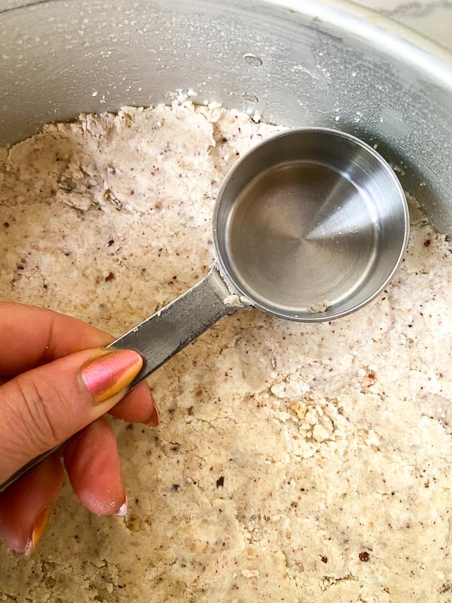 using measuring cup to press dough into pan