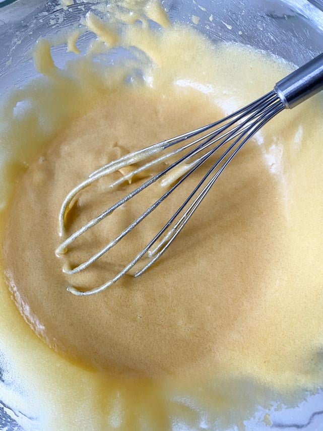 whisking eggs and egg yolks into melted butter and sugar in glass bowl