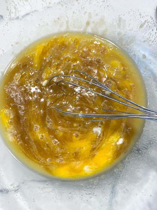 whisking eggs and yolk into butter and brown sugar in clear bowl