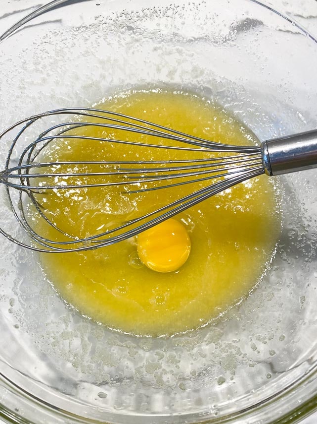 whisking eggs into butter sugar mixture in clear glass bowl