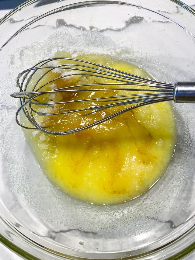 whisking sugar and vanilla extract into melted butter in clear glass bowl