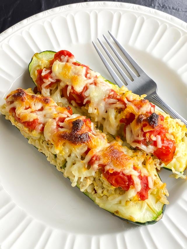 2 stuffed zucchini boats on a white plate with fork