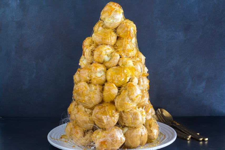 vertical image of croquembouche on white plate against dark background