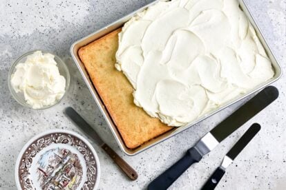 Swiss Meringue Buttercream on yellow cake in pan; icing spatulas alongside