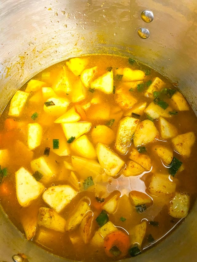 adding broth to pot filled with carrots, potatoes and patty pan squash cut into chunks for soup