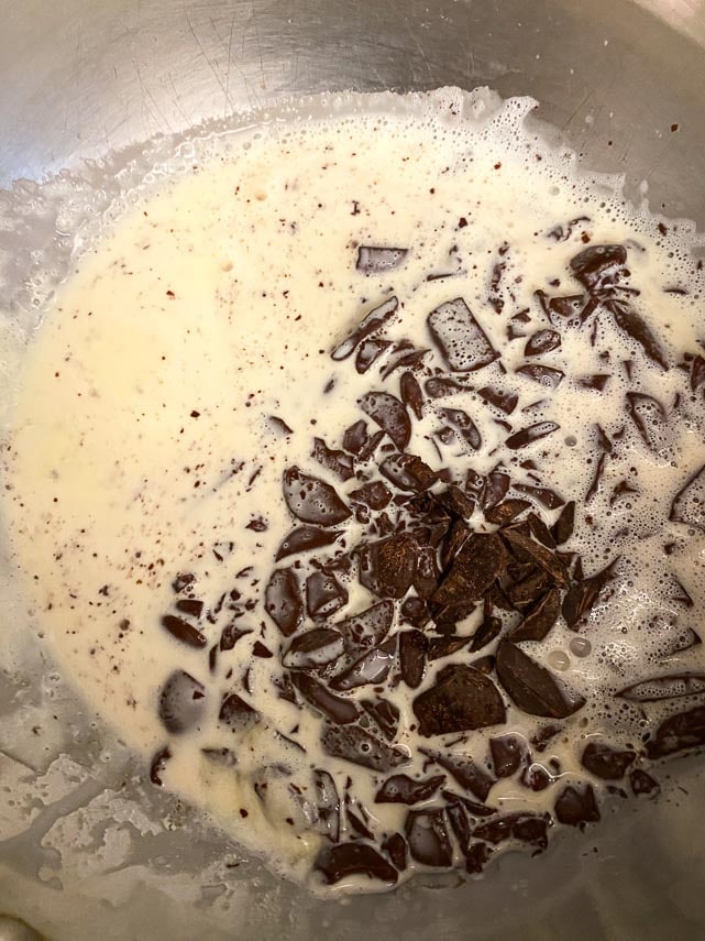 adding chopped dark chocolate to hot cream in pot