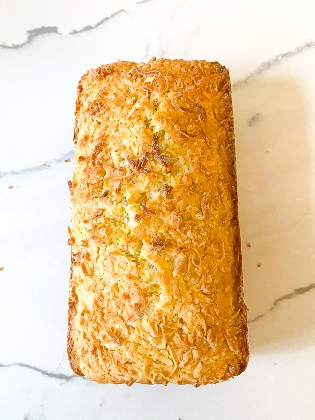 baked loaf of coconut lime bread, unmolded from pan on white marble surface