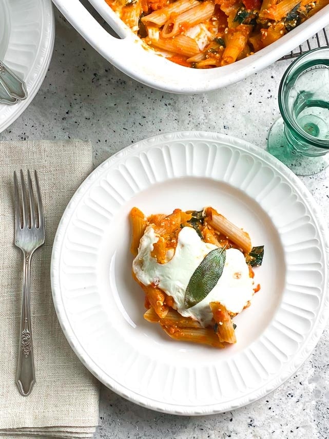 baked pasta with roasted pumpkin on white plate with fresh mozzarella and sage