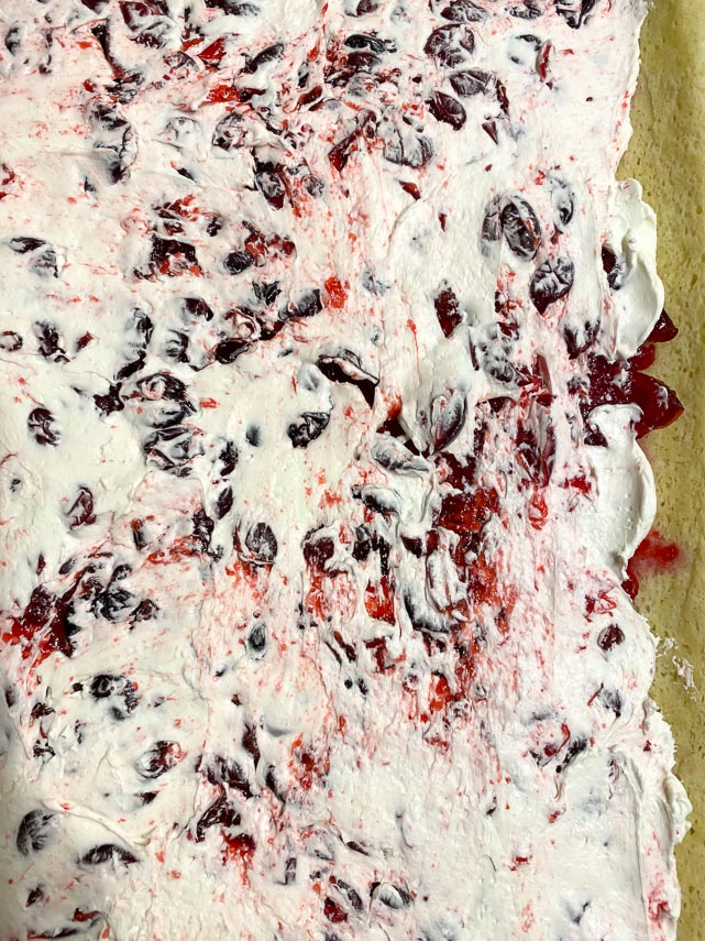 buttercream spread over cranberry filling on jellyroll sponge cake