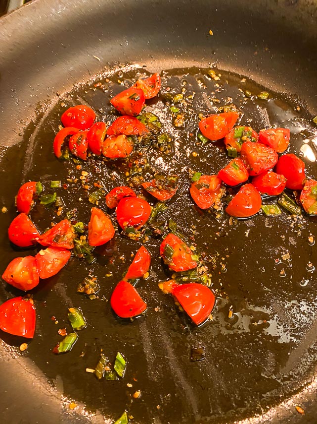 cherry tomatoes amd scallion greens sauteeing in pan with herbs and Garlic-Infused oil