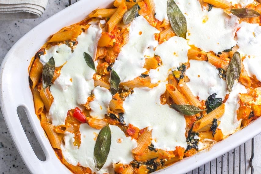 close overhead shot of baked pasta with roasted pumpkin, fresh mozzarella and sage in white baking pan on rack