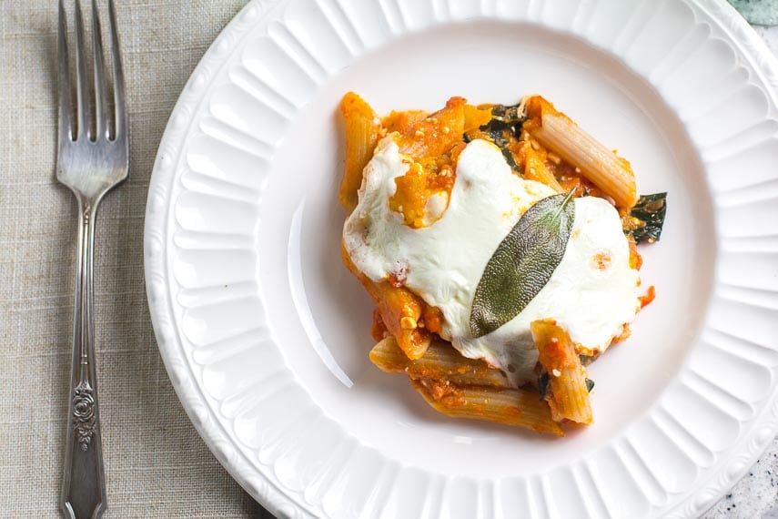 closeup of white plate holding serving of baked pasta with roasted pumpkin, fresh mozzarella and sage