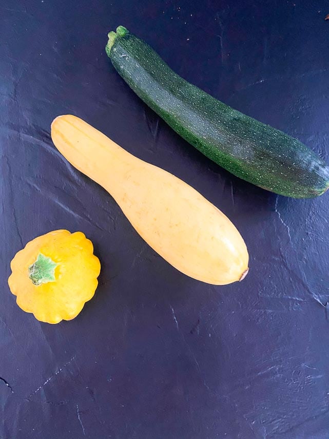 comparison image of zucchini, yellow summer squash and patty pan squash on dark background