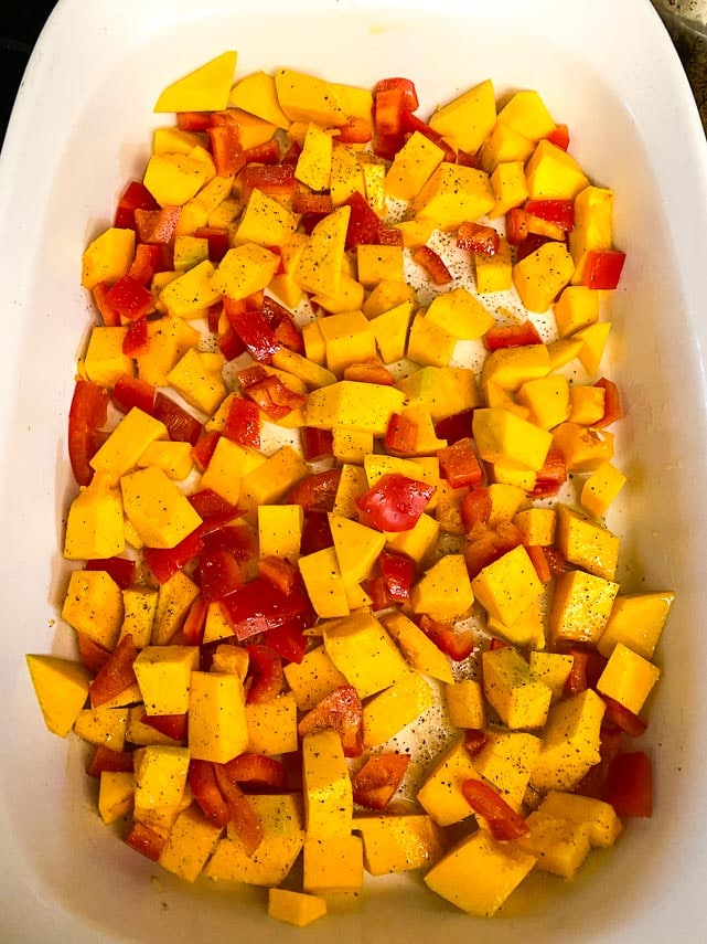 cubed squash and red peppers, coated with oil and seasoned with sal;t and pepper in a white baking dish
